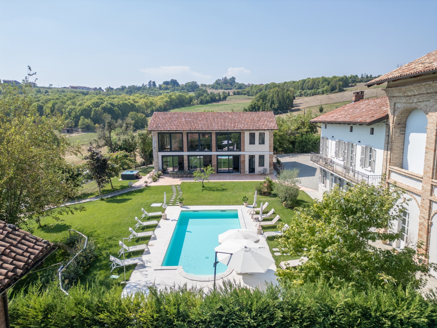 Aerial view of a restored Monferrato villa with new pool, garden and panoramic hill backdrop